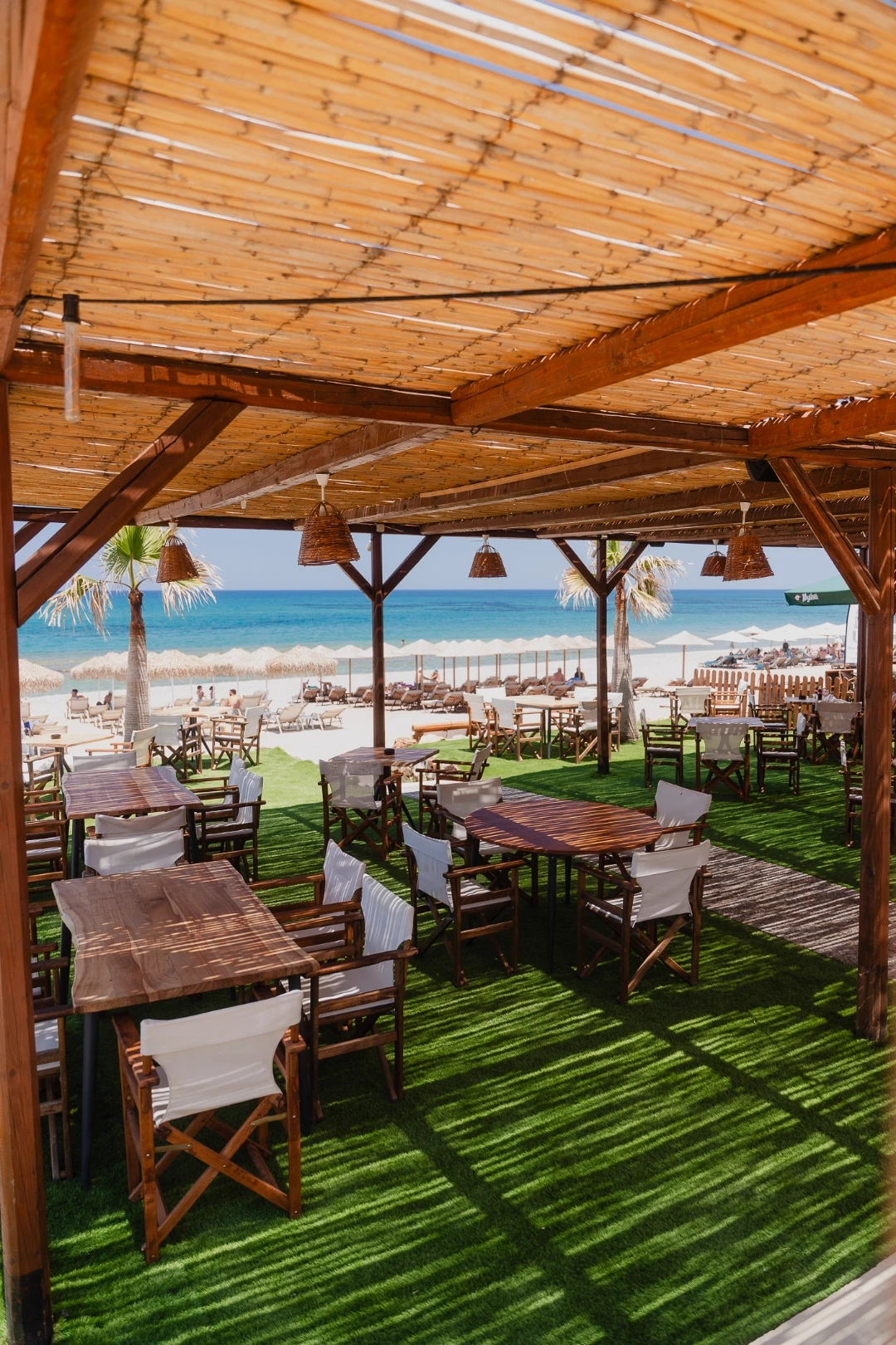 Beachfront dining terrace by day with tables, palm tree and sun loungers on the sand